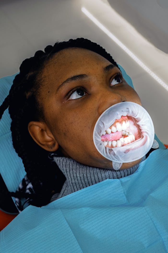 From above of African American woman with mouth expander sitting in dental chair in modern clinic and looking up pensively during procedure
